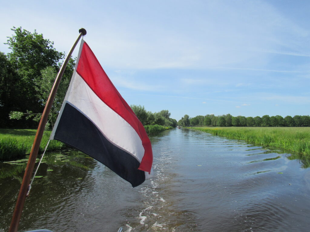 Dutch flag in foreground on back of boat travelling along canal