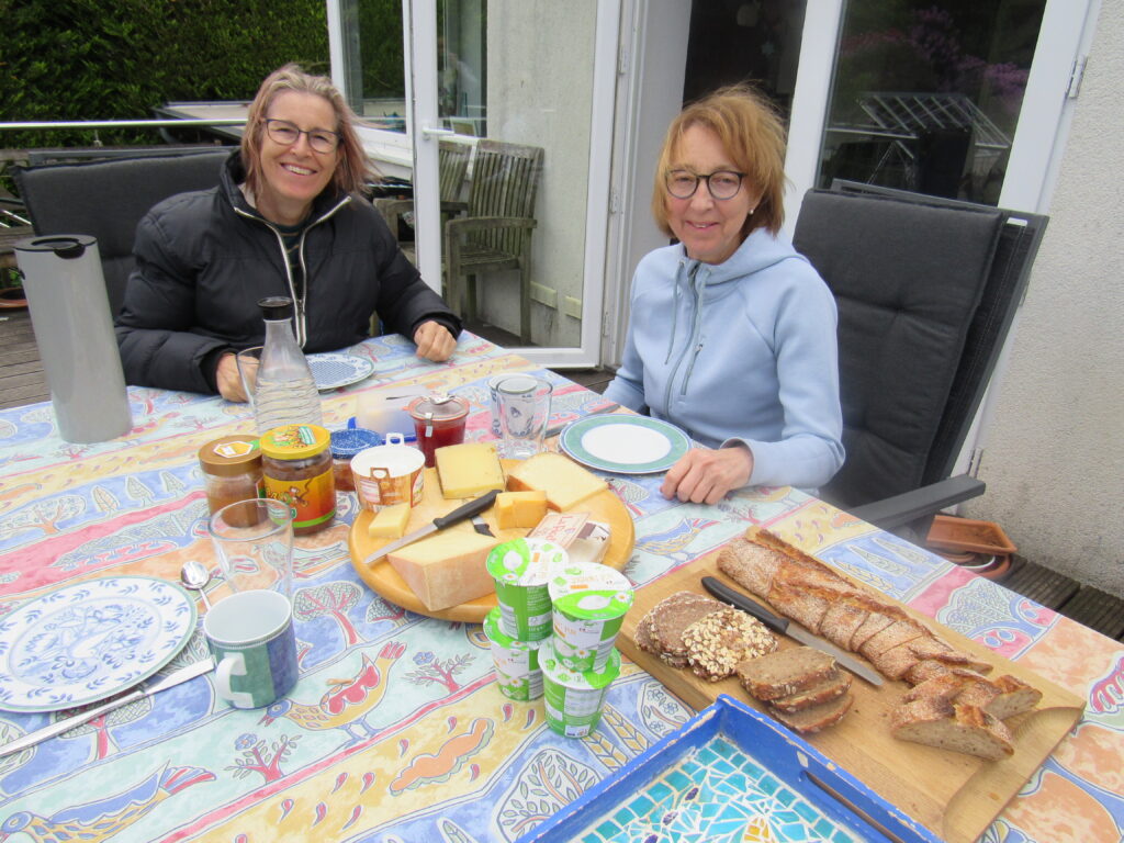 2 women sitting at a table that has lots of cheese and bread